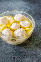 Glass bowl of labneh balls in oil, spiced with garlic and rosemary