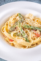 Tagliatelle pasta with creamy garlic sauce, asparagus, peppers, and parmesan topping