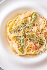 Tagliatelle pasta with creamy garlic sauce, asparagus, peppers, and parmesan topping