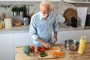 Happy retired senior man cooking in kitchen. Retirement, hobby people concept. Portrait of smiling senior man cutting vegetables.