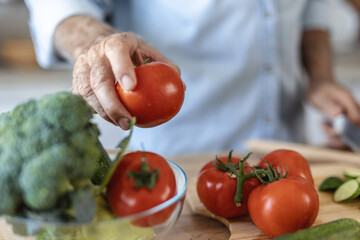 Senior man in kitchen cooking healthy meal. Handsome senior man is cooking in the kitchen and smiling while standing at table full with fresh colorful vegetables.