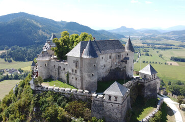 Aerial view of a medieval Hochosterwitz castle and church tower in the Austrian Alps. Stone walls, forest, and mountain landscape. European architecture and cultural heritage. Travel destination. 