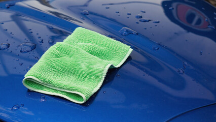 Shining Surface: A close-up shot of a vibrant blue car surface being meticulously cleaned with a soft, green microfiber cloth. The glossy finish reflects the light.