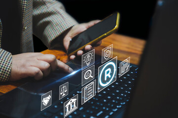 A person using a laptop and smartphone, with holographic icons floating above the keyboard,...