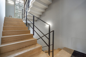 A contemporary staircase features warm wooden steps and sleek metal railings. Sunlight filters...