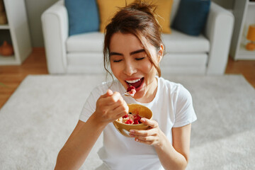 Smiling young woman enjoying a healthy breakfast of oatmeal with berries in her living room