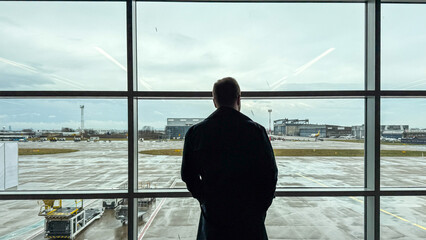 Fototapeta premium Solitary silhouette of a contemplative Caucasian man gazing at rain-drenched tarmac, evoking Samhain's introspective journey or melancholy transit