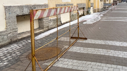 A rusty barricade guards a lonely manhole, echoing urban isolation, perfect for International...