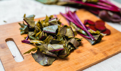 Fresh beetroot greens on a rustic table cloth and beet cuts on a cutting board. Process of preparing beetroot for cooking. Local food concept.