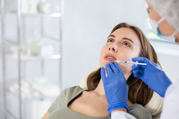 Closeup portrait of young long-haired female patient having lips injection at treatment room of...