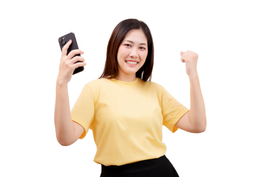 Asian young beautiful smiling woman in a yellow shirt holds a smartphone and raises her fist in a celebratory gesture.