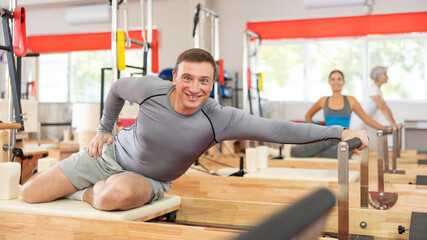 Visitor of fitness club is engaged in Pilates simulator. Improvement of well-being, physical...