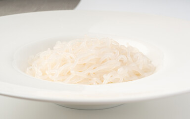 Shirataki or konnyaku pasta in white plate close up. Konjak jelly noodles
