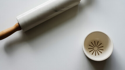A minimalist still life photograph of a white marble rolling pin and a white ceramic citrus juicer on a pure white surface