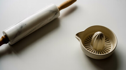 A minimalist still life photograph of a white marble rolling pin and a white ceramic citrus juicer on a pure white surface