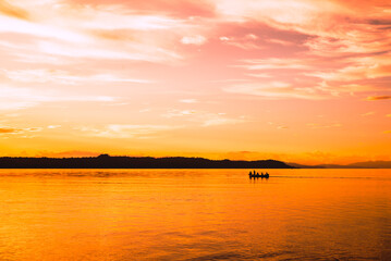 Naklejka premium Sunset on the beach with the silhouette of mountains and fishermen with their boats at sea