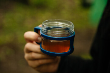 hand holding plastic mug with tea in the forest, travel