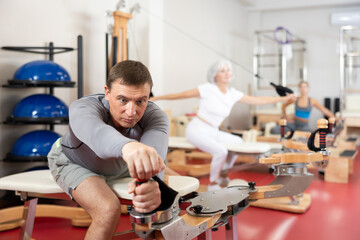 In gym, male performs Pilates exercises to lose weight and bring muscles of arms, chest, and body...