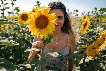 Young woman holding a sunflower on the sunflower field with blue sky.