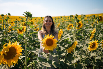 Young woman holding a sunflower on the sunflower field with blue sky.