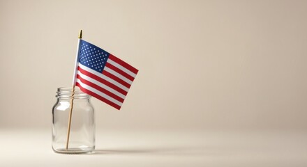 Fototapeta premium A small american flag proudly sits in a glass jar on a neutral, minimalist background.