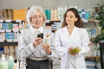 Mature woman scans mobile barcode of medical-grade shampoo for hair restoration at pharmacy. Woman pharmacist helps a pensioner pay for purchases using a QR code