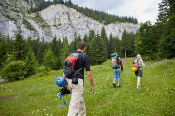 Hikers approach rocky mountainside on a summer day in a lush green landscape