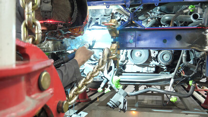 A Welder Welds a Car Frame on a Straightening Rack at Car Shop in Repair Process. Restoration of Damaged Frame of the Car on a Special Rack 
