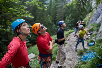 Climbers prepare for an ascent while studying a rock face in a forested area