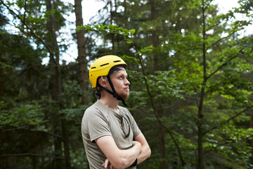 Man wearing a yellow helmet stands in a forest while contemplating nature in the afternoon