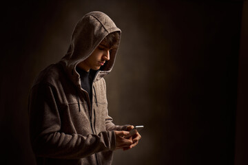 Young man wearing hoodie using smartphone in dark room