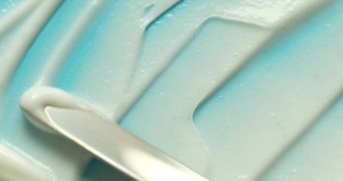 Making skincare cosmetic product smears with metal spatula on blue background close up. Beauty abstract