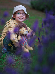 Preschool boy with glasses and panama hat holding handmade soft toy in hands squatting in lavender...