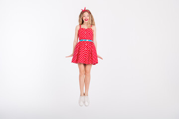 Joyful woman in a red vintage polka dot dress expressing happiness while jumping on a white background