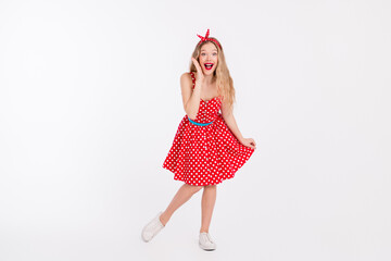 Smiling young woman wearing a red polka dot dress posing enthusiastically, expressing joy and confidence on a white background.