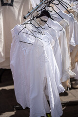 White clothing hanging on hangers at outdoor market stall