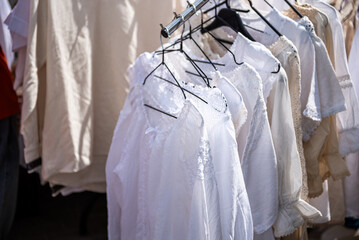 White clothing hanging on hangers at outdoor market stall