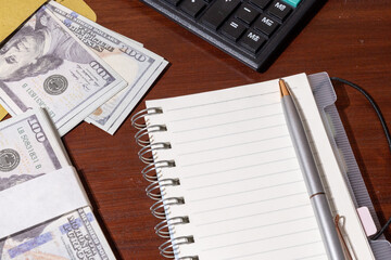 A minimal desk setup showing cash placed beside a notepad and calculator, representing financial...