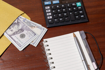 A minimal desk setup showing cash placed beside a notepad and calculator, representing financial...