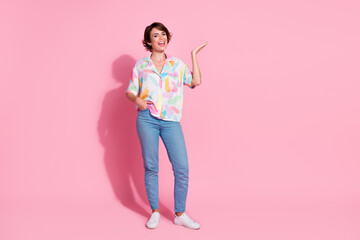 Full length portrait of nice young lady arm hold empty space wear shirt isolated on pink color background