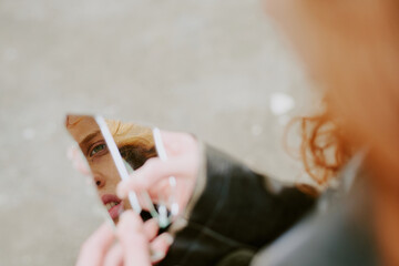 Female holding fragment of broken mirror displaying reflection in unclear outdoor environment....