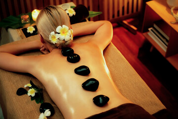 Hot stone massage at spa salon in luxury resort with warm candle light, blissful woman customer...