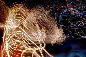 Abstract long exposure light trails forming golden strands and vivid color bursts, captured through...