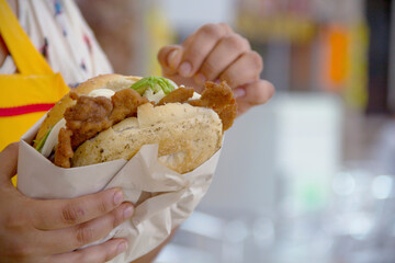 Mexican torta filled with beef milanesa, avocado, and Oaxaca cheese held by young Latina woman at a local market.