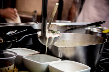 Close-up of steaming seafood chowder ladle over bowls in a busy professional kitchen, capturing the dynamic cooking environment. Perfect for culinary, restaurant, and food service marketing.