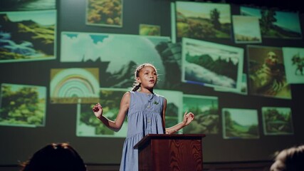 Illuminated by spotlights, a young girl stands at a podium, passionately delivering a speech about environmental conservation against a backdrop of nature themed projections