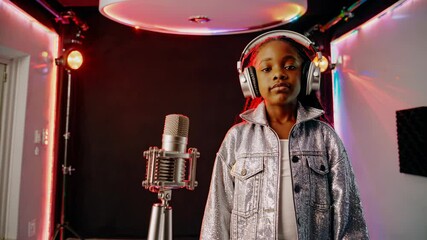 Professional recording studio setting capturing young performer adjusting headphones, surrounded by vibrant neon lights, preparing to record music with confident energy