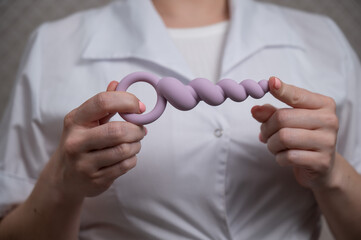 Woman in doctor's coat holding anal beads. 