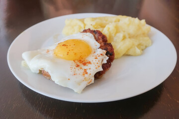 beefsteak with egg and mashed potatoes on a white plate on a wooden table