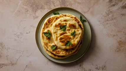 A top-down view of stacked flatbreads on a matte gray ceramic plate against a textured beige stone surface.